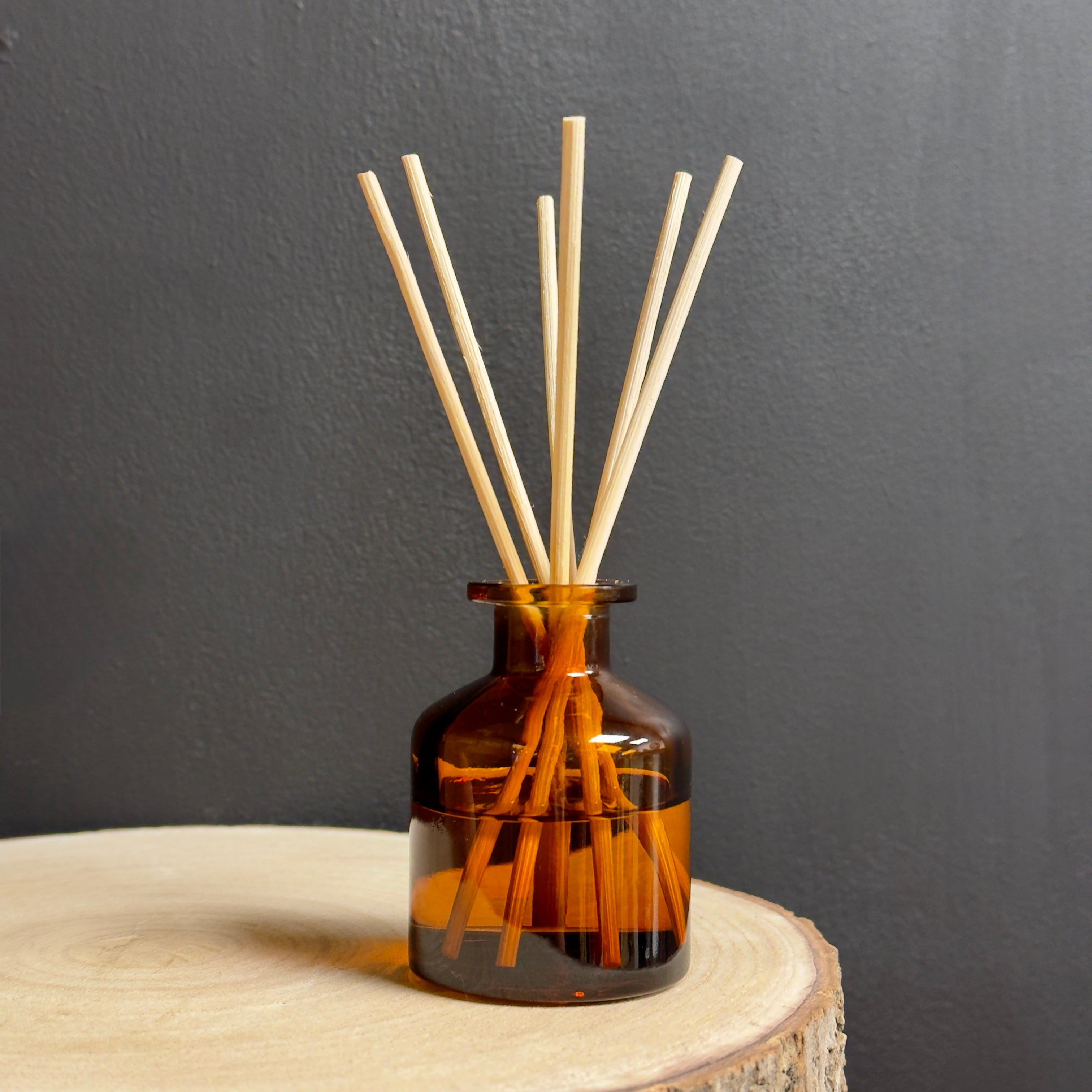 Brown glass diffuser bottle with wooden sticks on a dark gray background