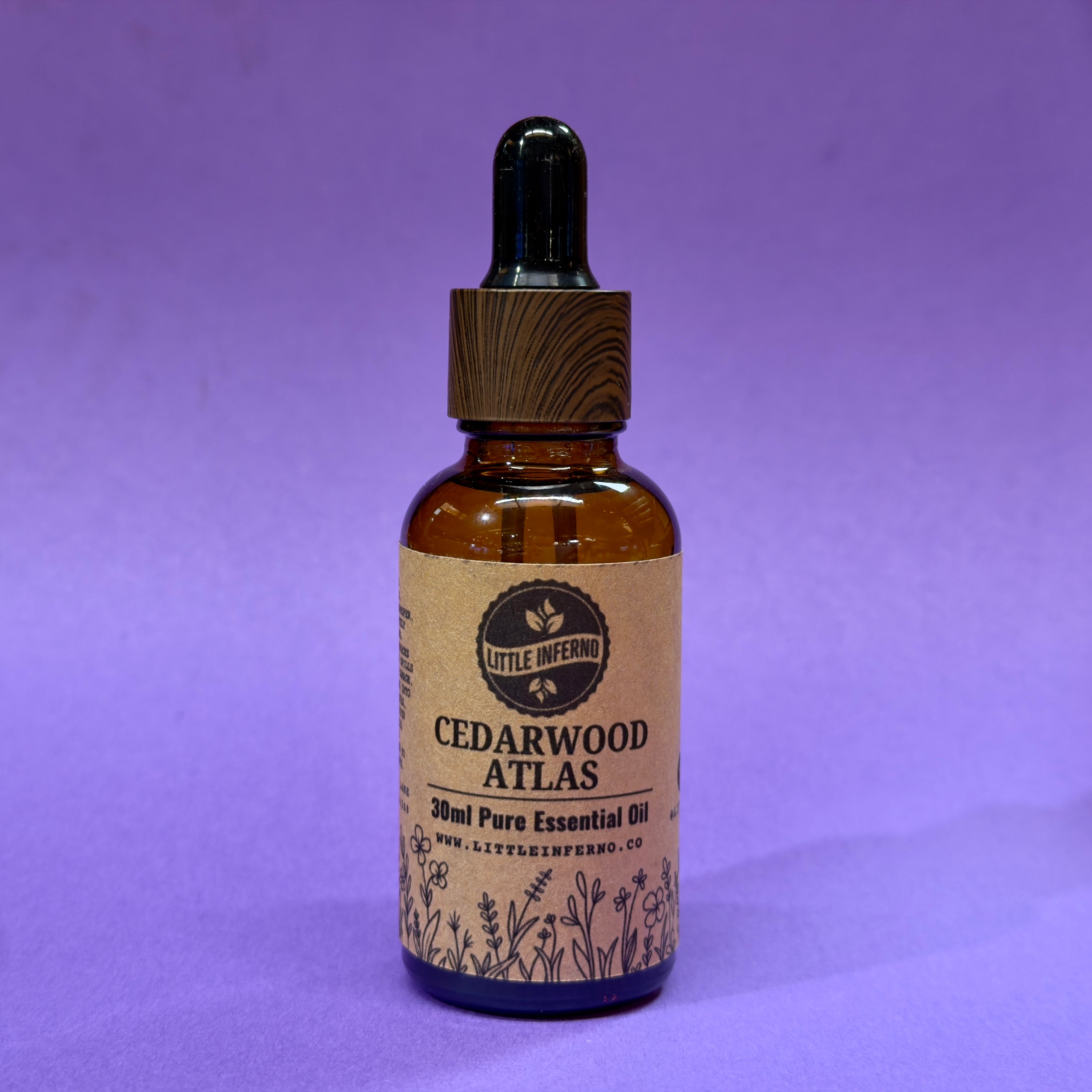 Bottle of Cedarwood Atlas essential oil with a wooden dropper on a purple background