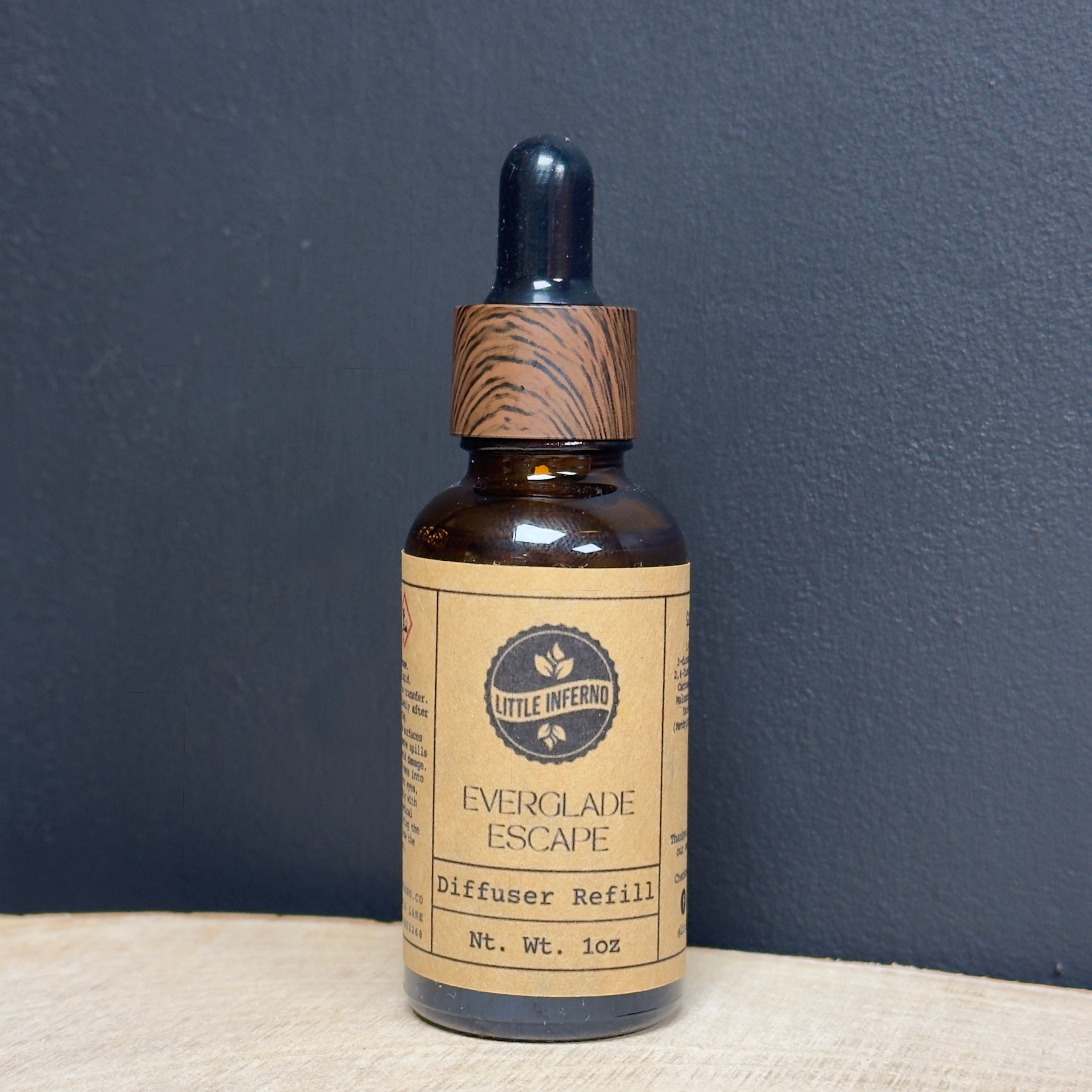 Bottle of 'Everglade Escape' diffuser refill with a wooden dropper on a dark blue background
