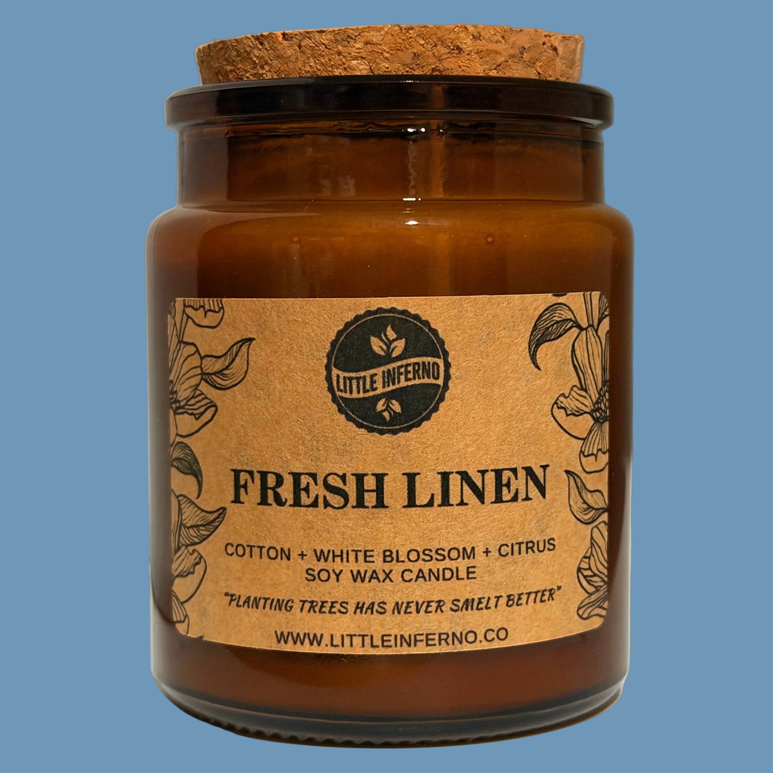 A soy wax candle in an amber glass jar with a cork stopper, featuring a kraft paper label that reads 'FRESH LINEN' and 'Little Inferno'.