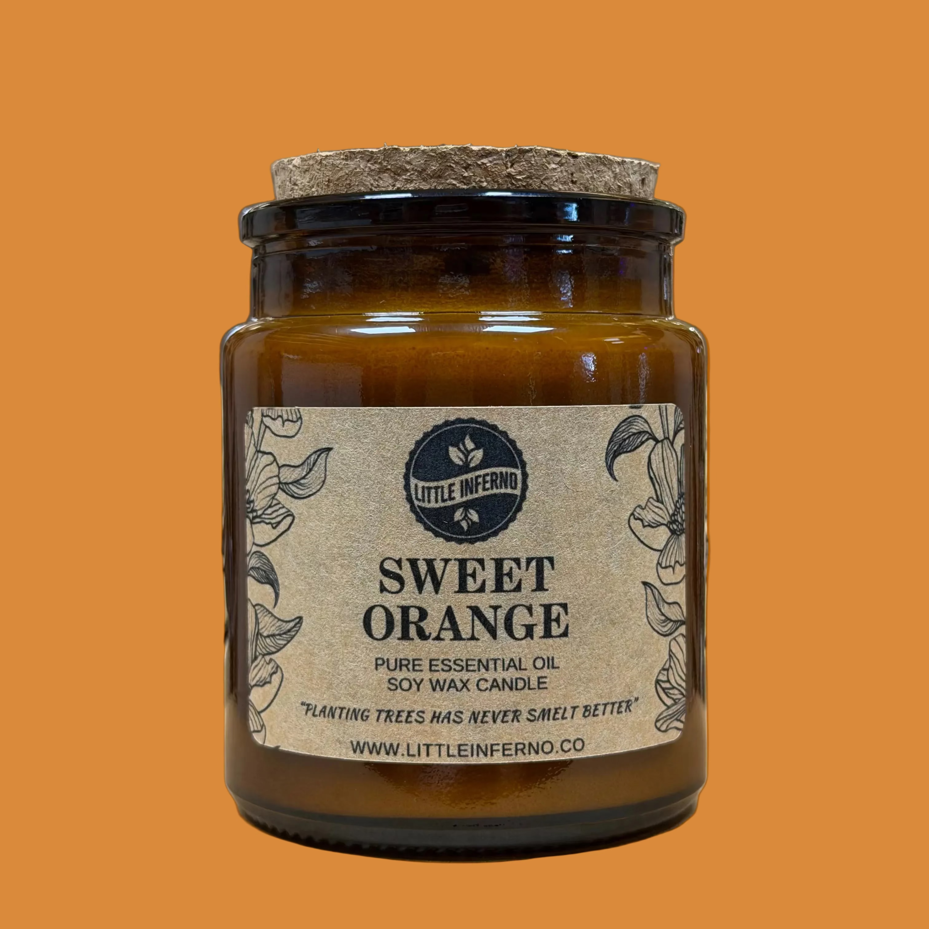 A Little Inferno 'Sweet Orange' soy wax candle in an amber glass jar with a cork lid, set on a wooden surface with a softly blurred shop background.