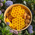Yellow honeycomb and round candies in a bowl surrounded by green leaves and purple flowers