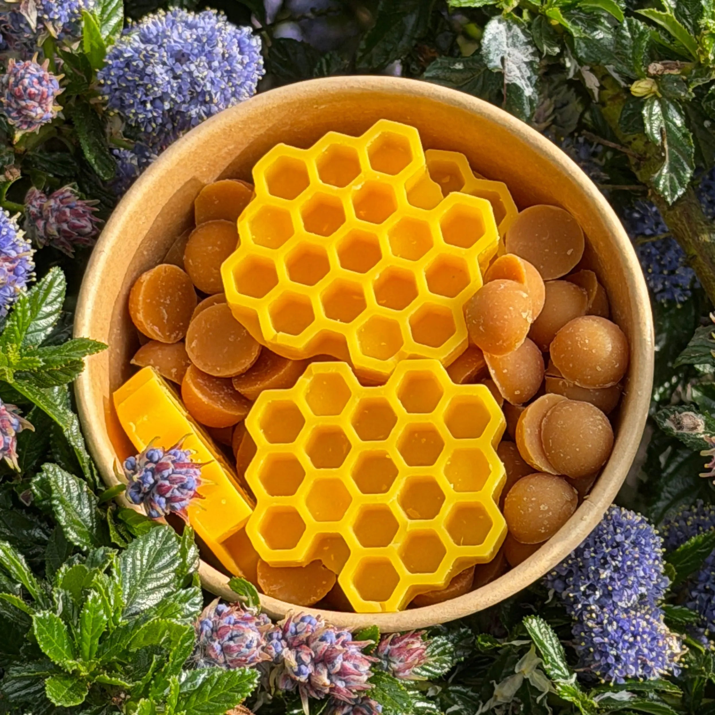 Yellow honeycomb and round candies in a bowl surrounded by green leaves and purple flowers