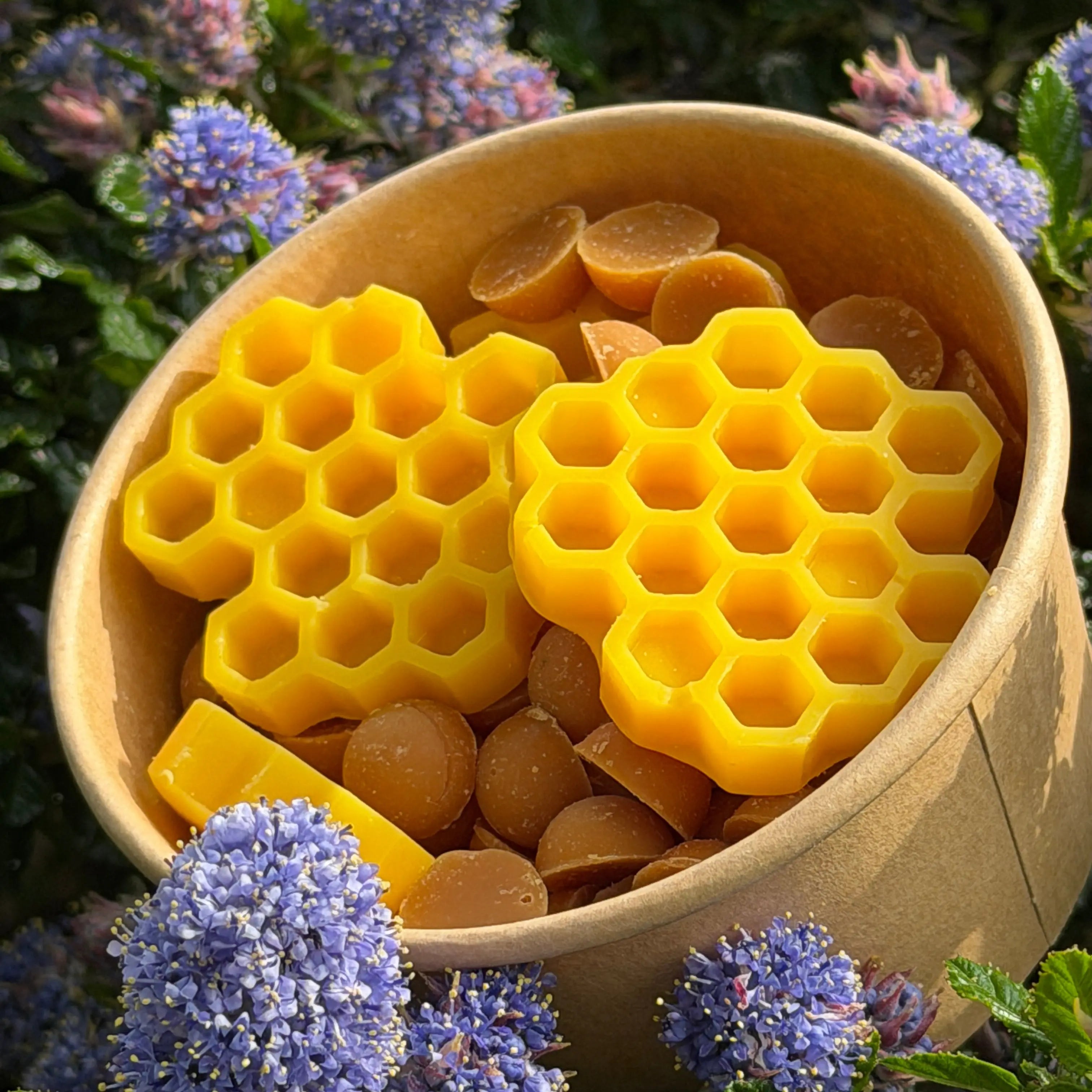 Beeswax honeycomb and beeswax balls in a container with purple flowers in the background