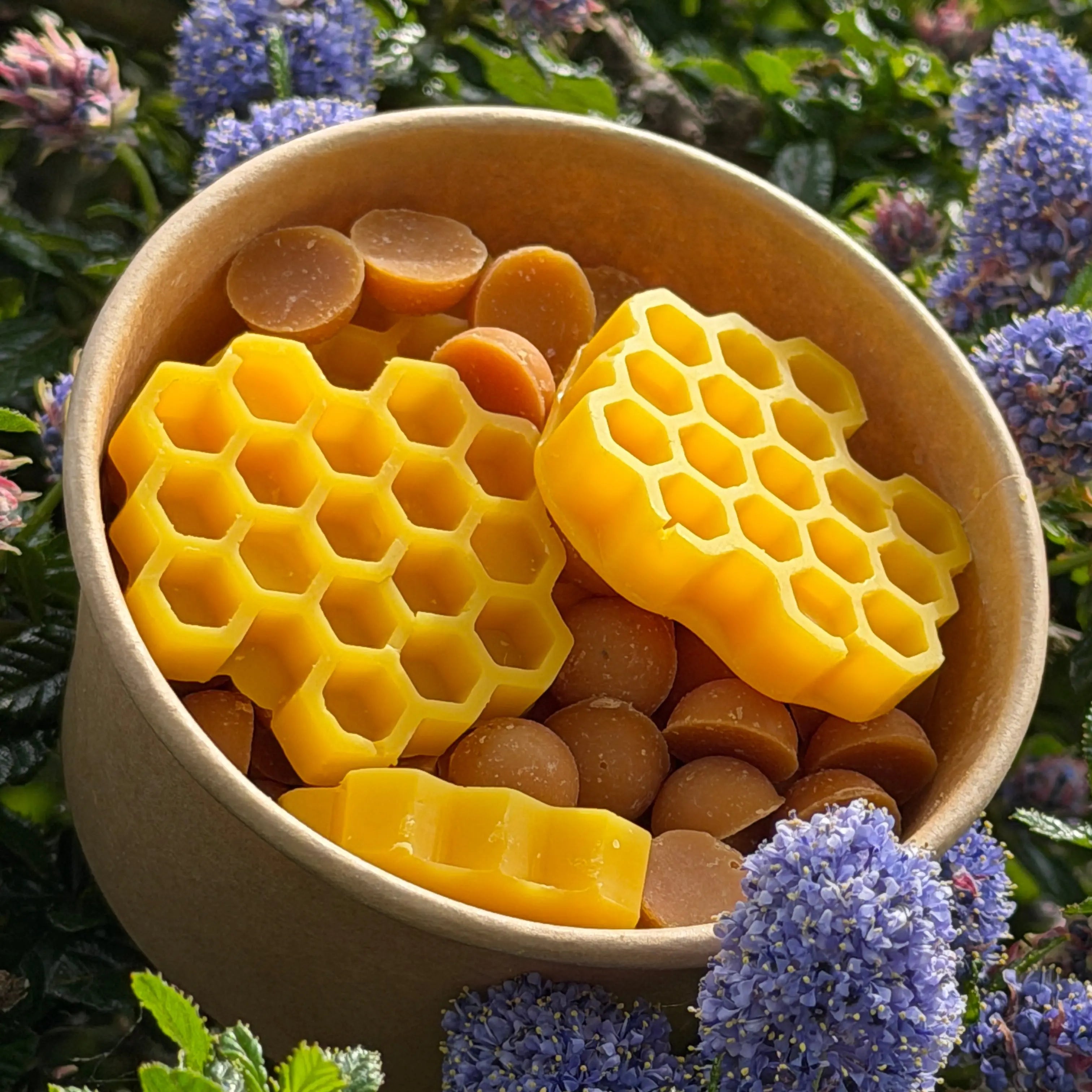 Bowl with honeycomb and round candies surrounded by purple flowers