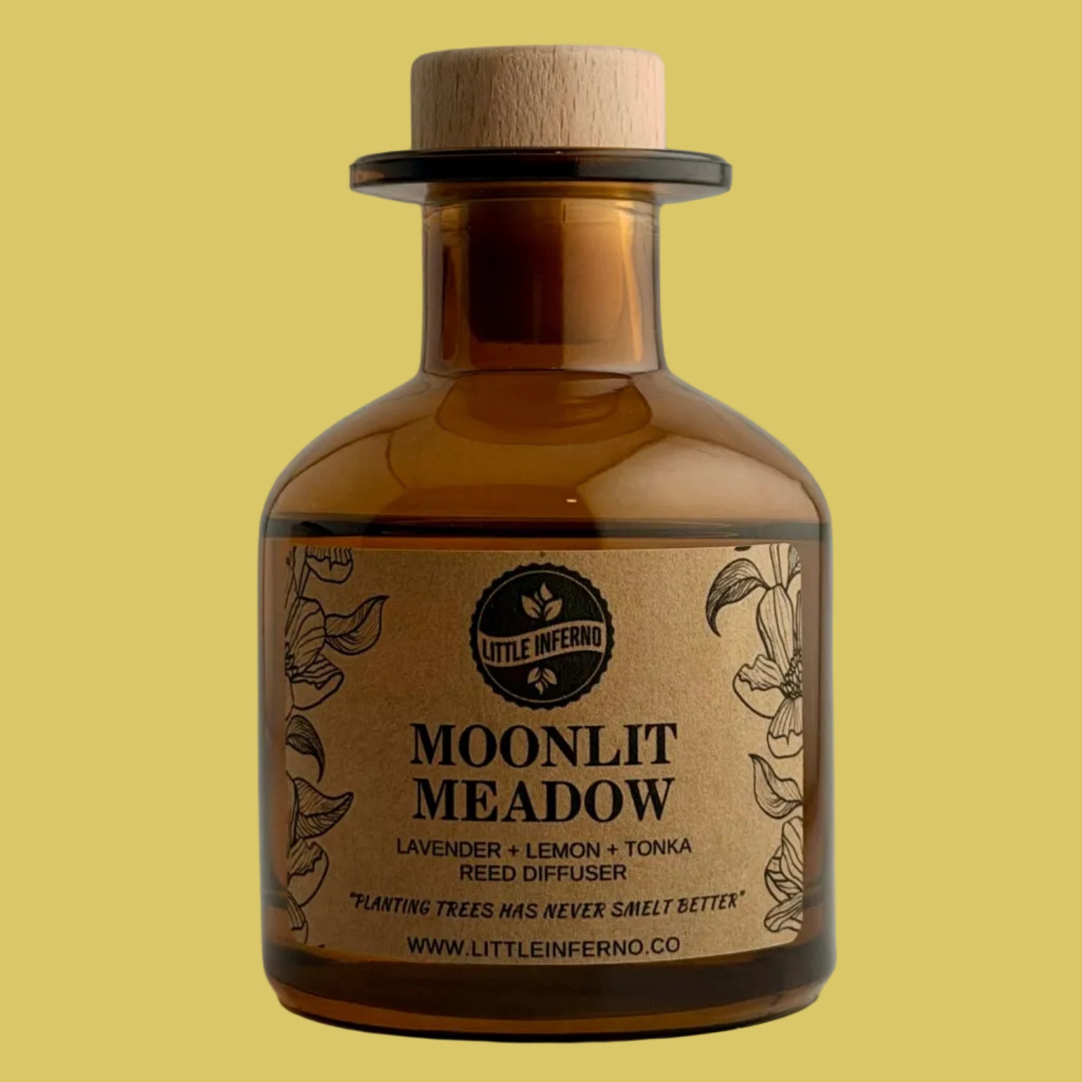 An amber glass reed diffuser bottle with a light wood cork stopper and a tan paper label reading 'MOONLIT MEADOW' by Little Inferno, photographed against a plain light gray background.