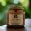 Candle jar with cork lid and 'Little Inferno' label on a wooden surface with a blurred green background