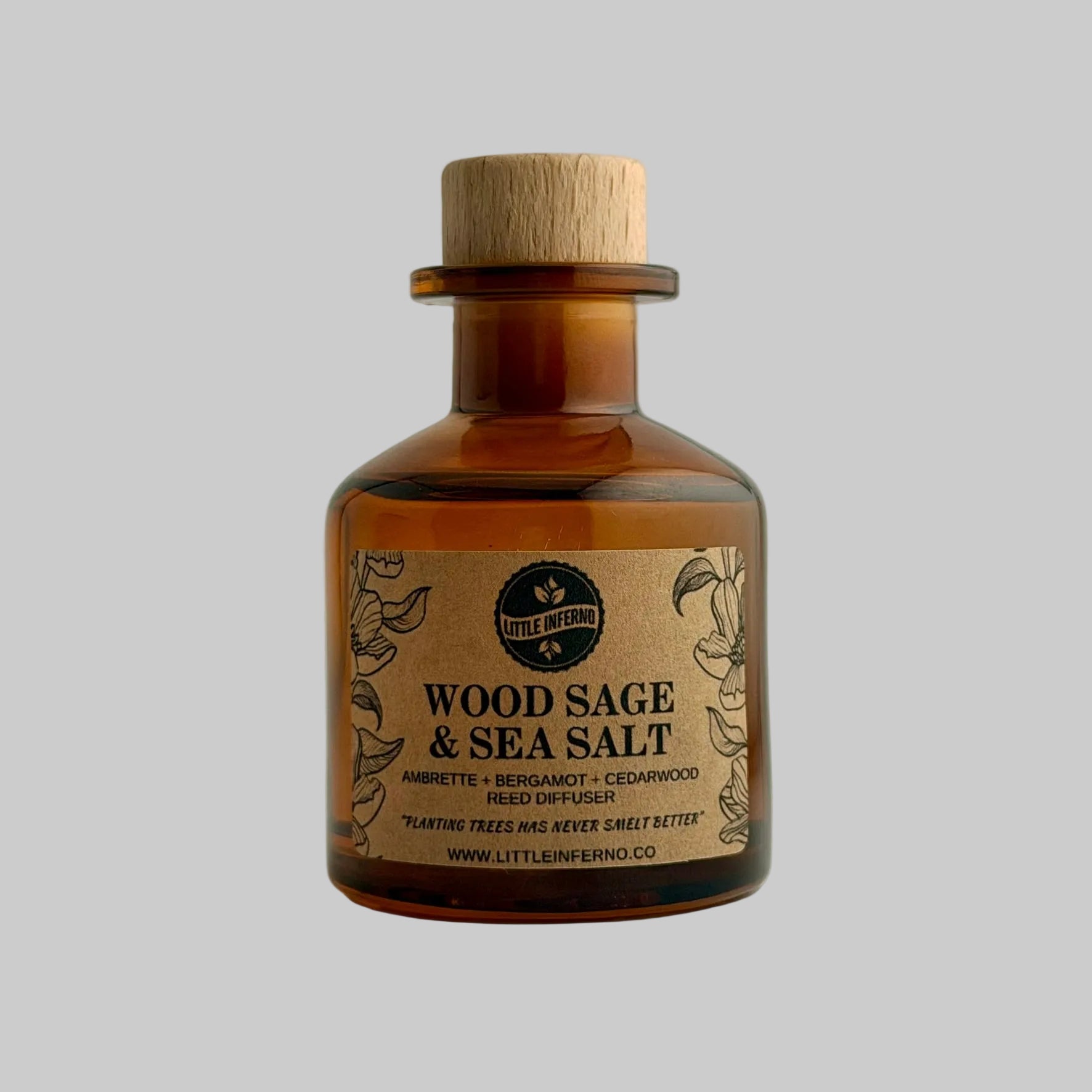 An amber glass bottle of Little Measured Wood Sage & Sea Salt with a natural wood cork stopper and a kraft paper label, set against a plain light gray background.