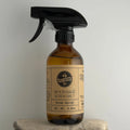 Brown spray bottle with black nozzle labeled 'Wood Sage & Sea Salt' on a gray background