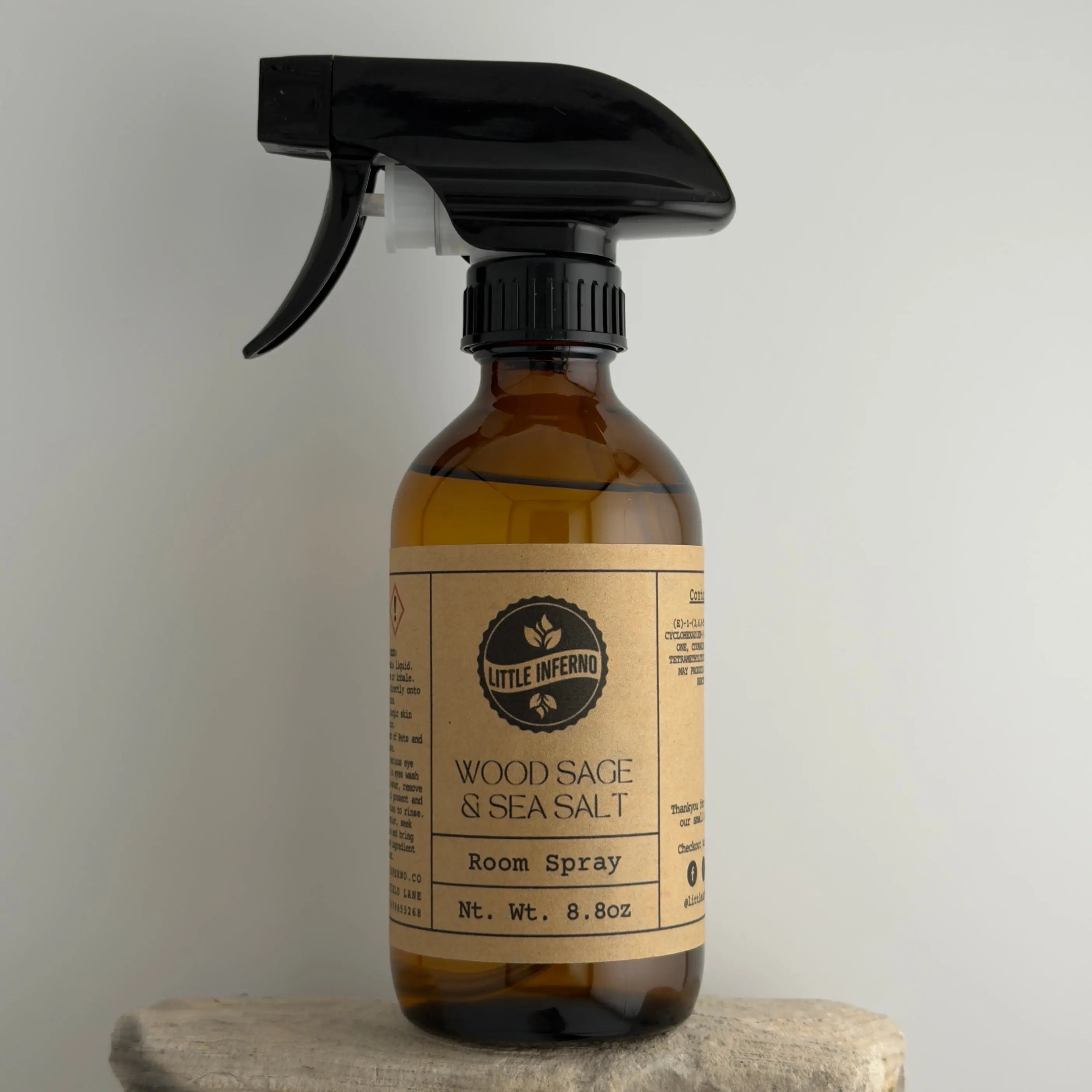 Brown spray bottle with black nozzle labeled 'Wood Sage & Sea Salt' on a gray background