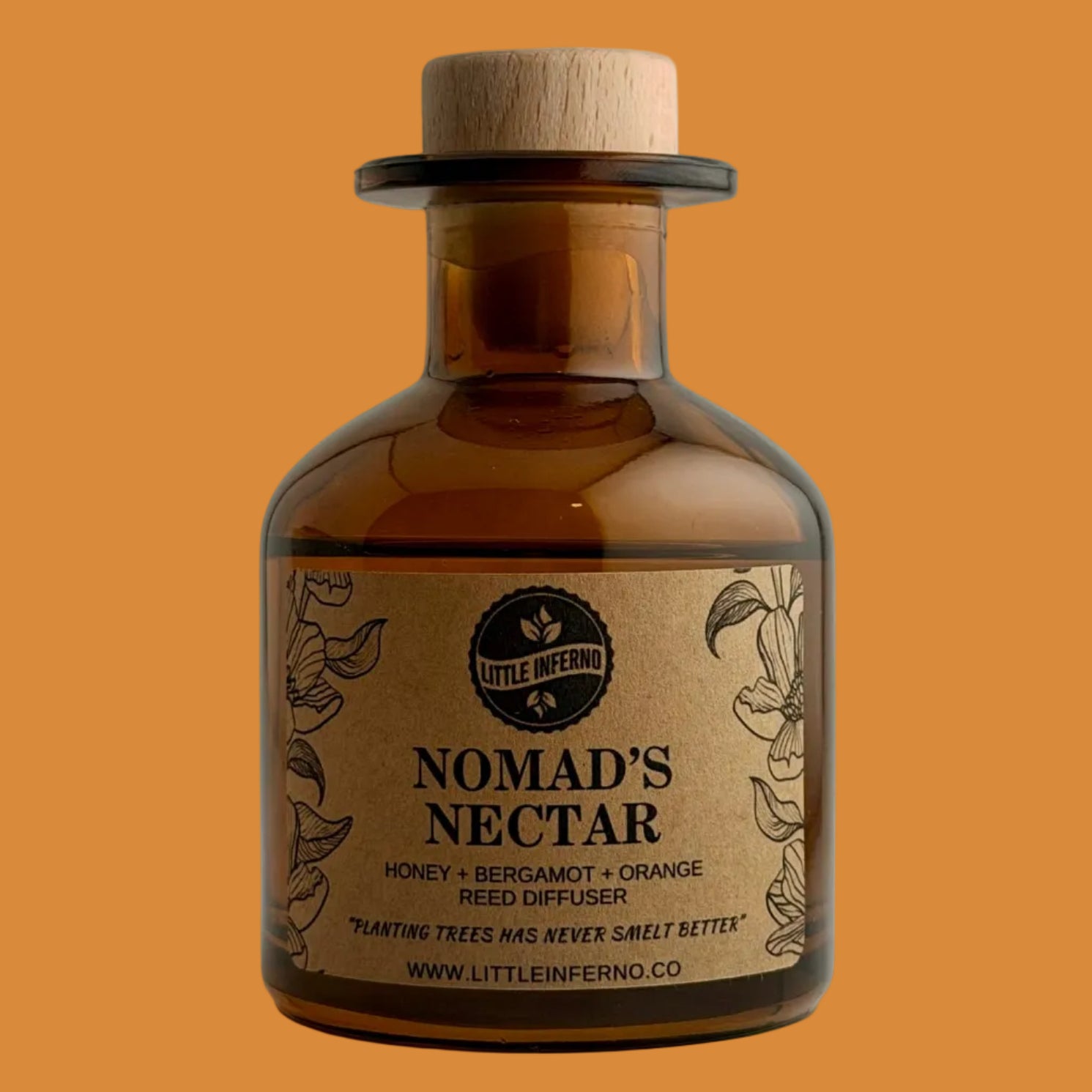 An amber glass reed diffuser bottle with a natural wood cork stopper and a kraft paper label reading 'NOMAD'S NECTAR' by Little Inferno, photographed against a neutral light gray background.
