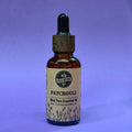 Bottle of patchouli essential oil with a dropper on a purple background