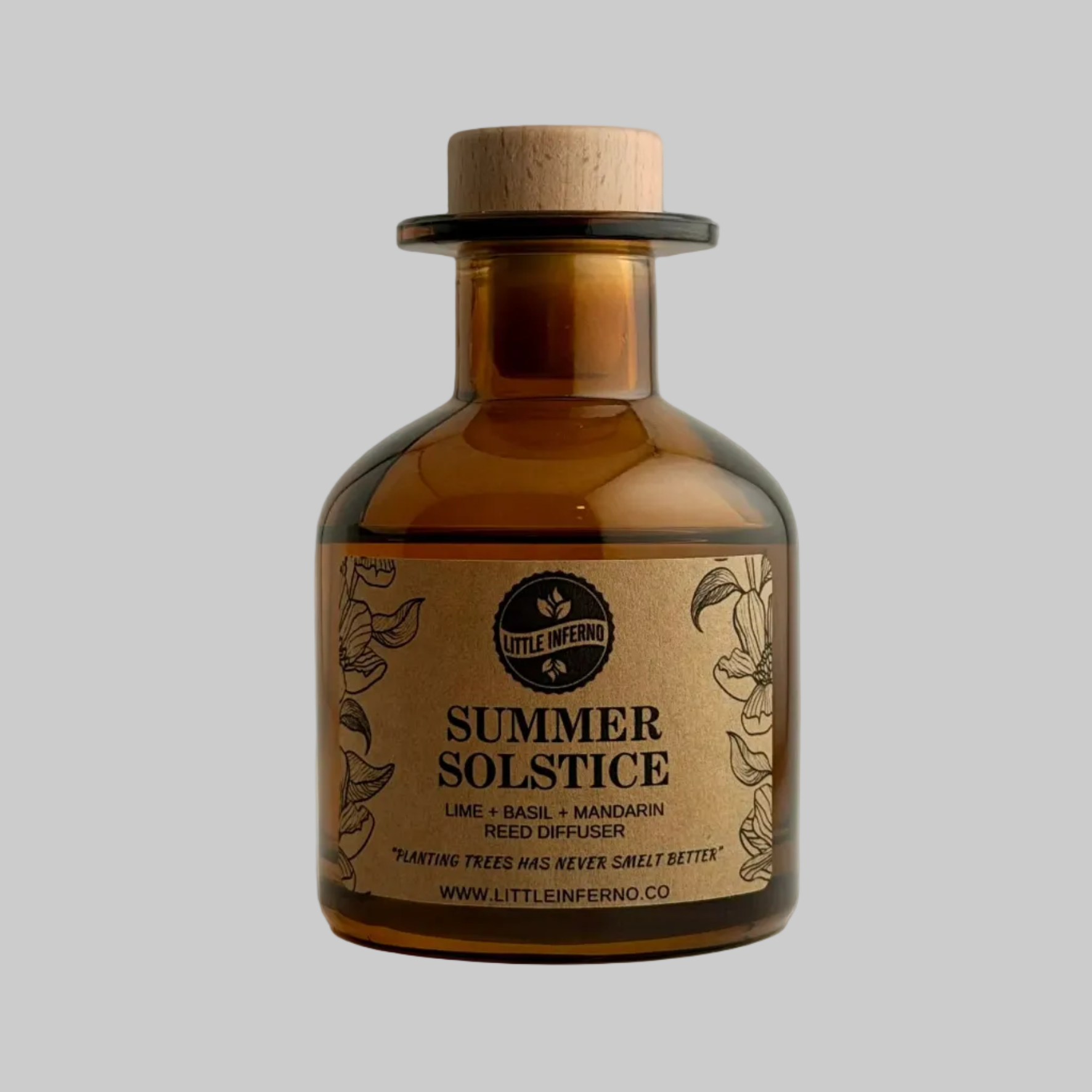An amber glass reed diffuser bottle with a cork stopper and a beige paper label reading 'SUMMER SOLSTICE' by Little Inferno, photographed against a plain light gray background.