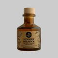 A small amber glass diffuser bottle with a light wood cap and a kraft paper label reading 'SUMMER SOLSTICE' by Little Measured, photographed against a plain light gray background.